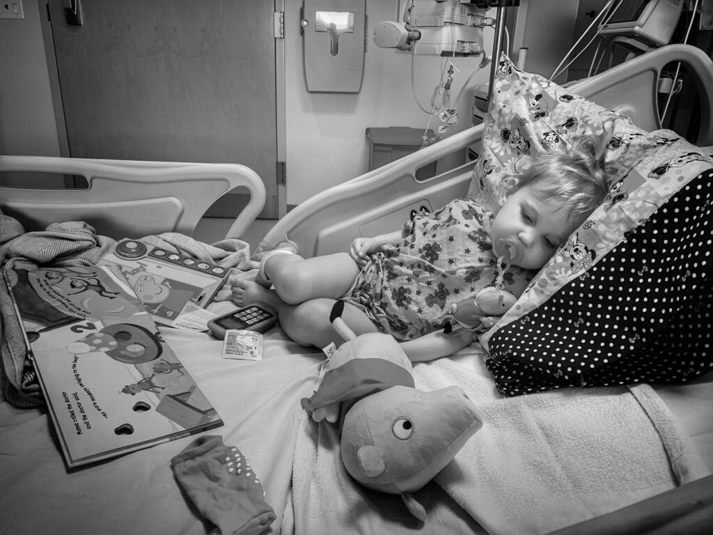 Mars lays on her hospital bed after being admitted to Phoenix Children's. She's surrounded by Peppa Pig books and toys. 