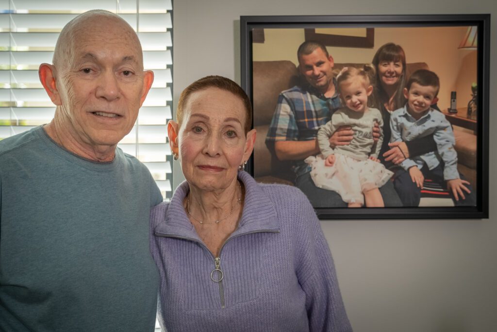 Howard and Pearl stand near a framed photo of their daughter and her children.