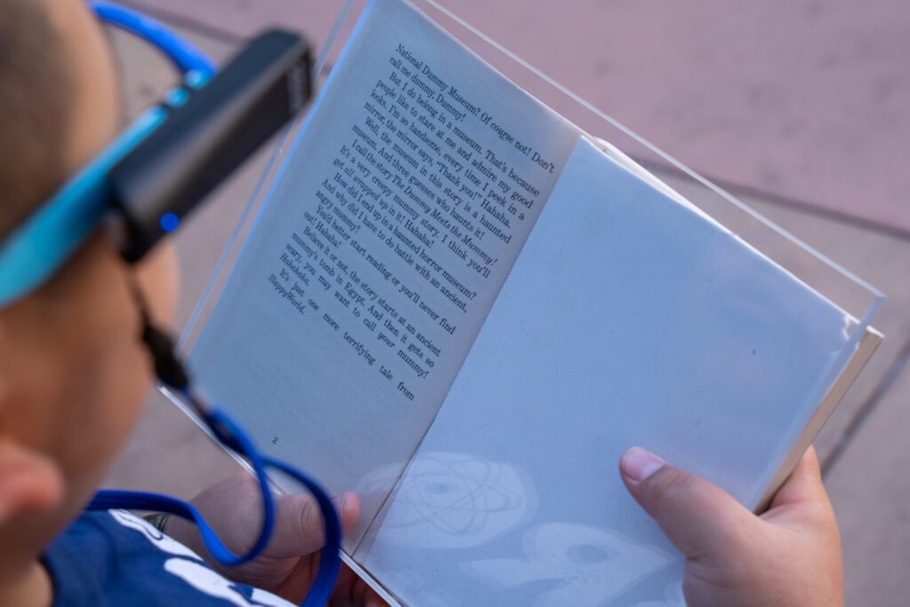 An image of the text of Chrisitan's book. He has a plastic slate covering over the book that helps his glasses read the text