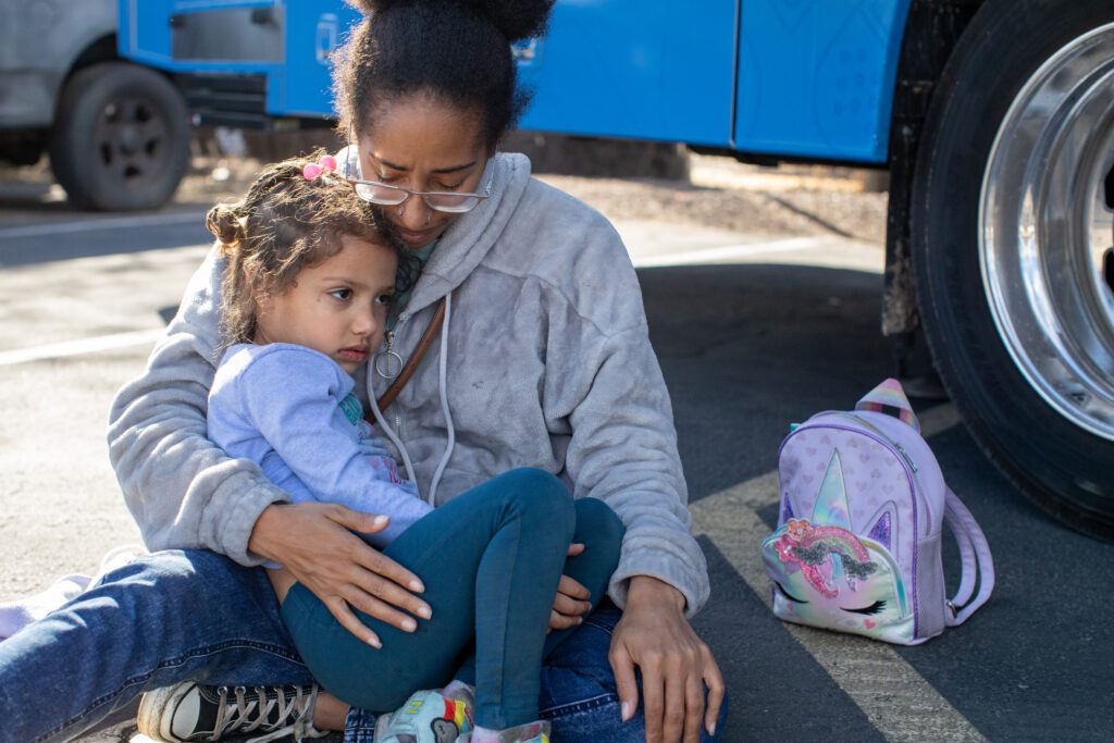 A mother holds her daughter in her arms. They are sitting outside Phoenix Children's Homeless Youth Outreach mobile medical unit. 