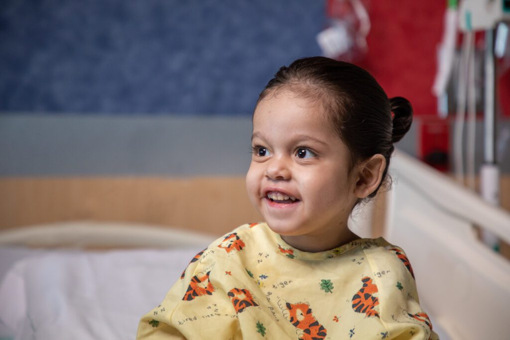 Namiko smiles. She is sitting on her hospital bed at Phoenix Children's. 