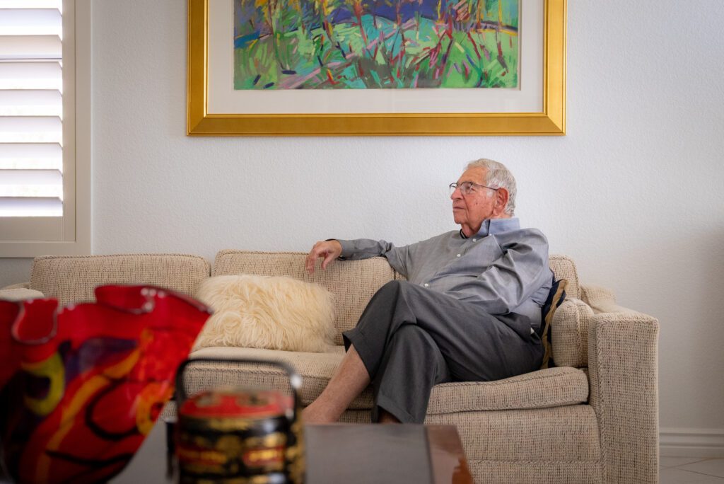 Dr. Winograd sits on his couch and looks off to the side of the room in an introspective way. 