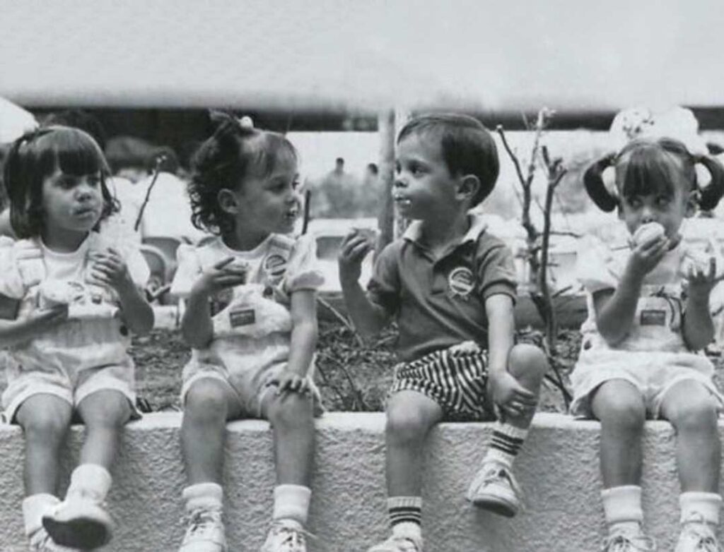 Four kids sit on a wall eating ice cream