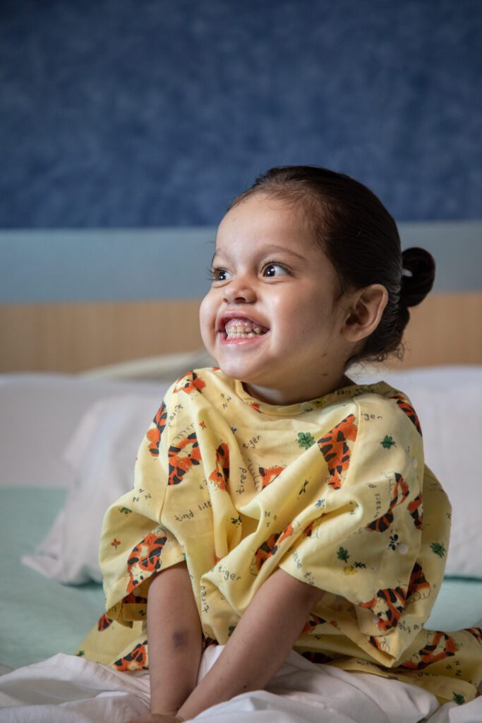 Namiko smiles wide for the camera. She is in her hospital room at Phoenix Children's. 