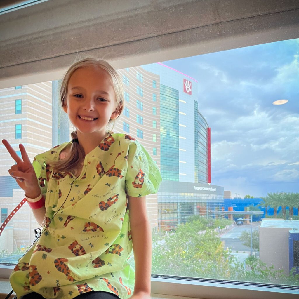 Sutton poses for a photo near her hospital room window. She's wearing her hospital gown
