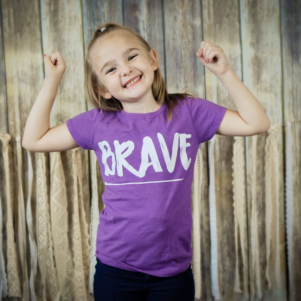 Sutton flexes her muscles as she wears a purple shirt that says "Brave"