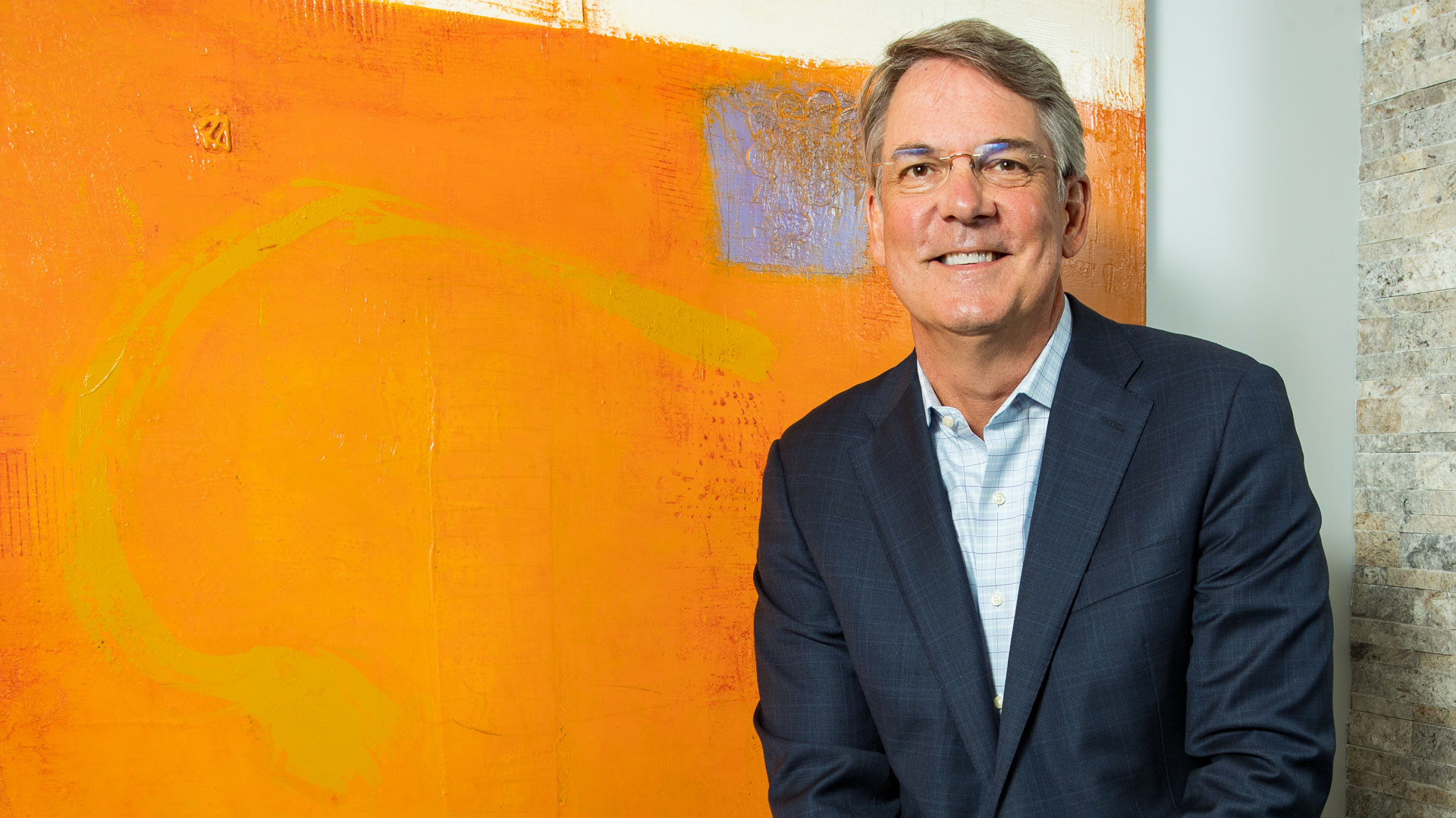 Chris Koch poses in front of an orange background at his office.