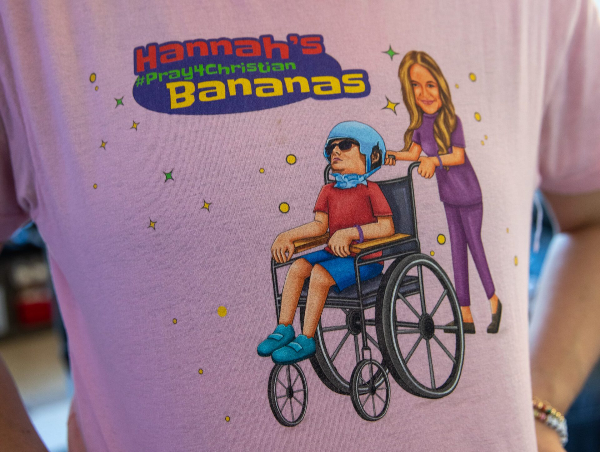 A close up shot of the graphic on Hannah's t-shirt. Its of Hannah in purple scrubs and she pushes Christian in his wheelchair. The shirt reads "Hannah's Banana's"
