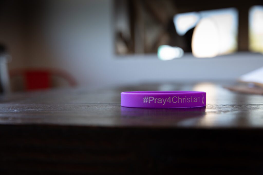 A purple bracelet that says Pray for Christian rests on a table