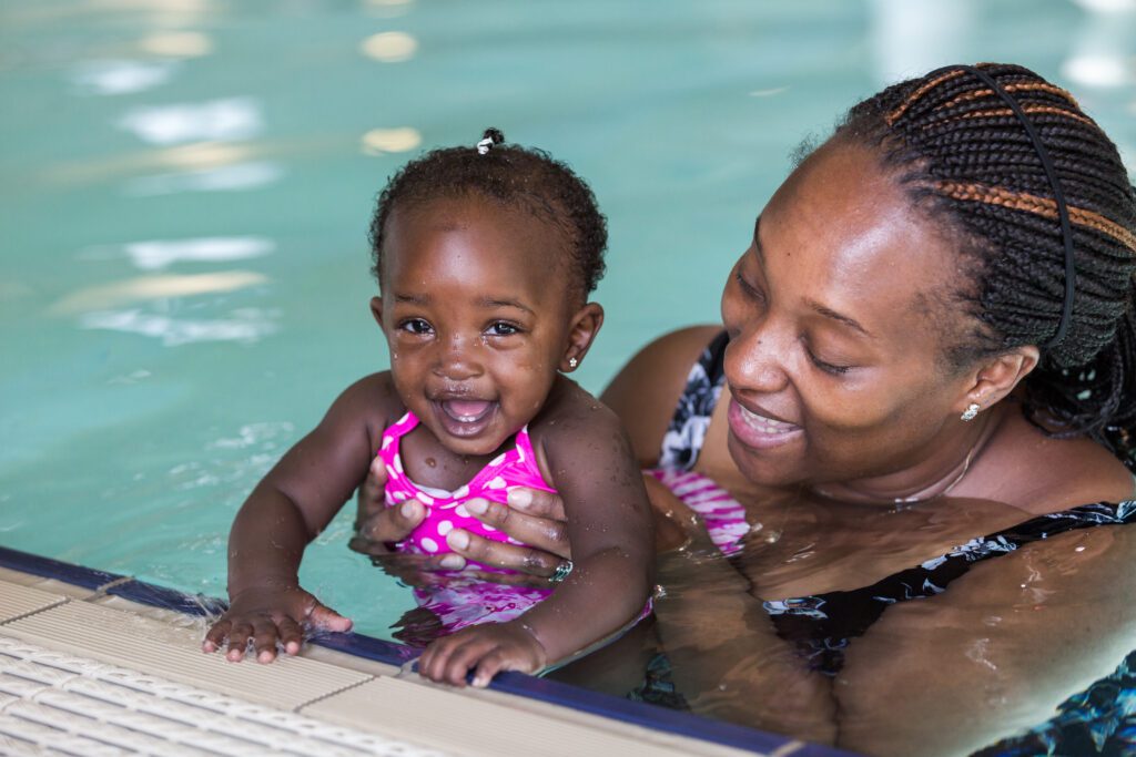 A mother holds her baby in an indoor swimming pool.
