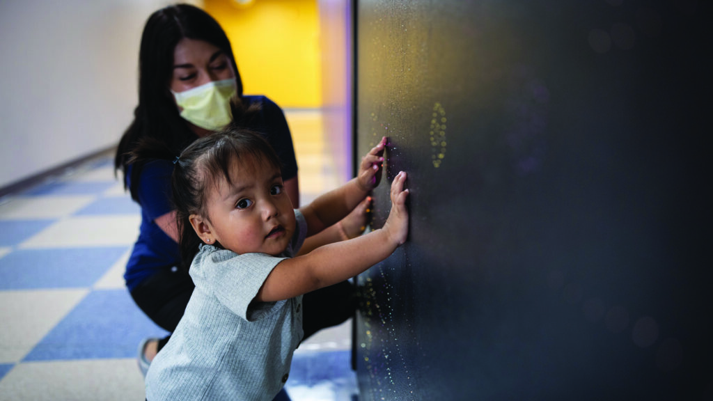 A small child leans against a wall in a hospital corridor.