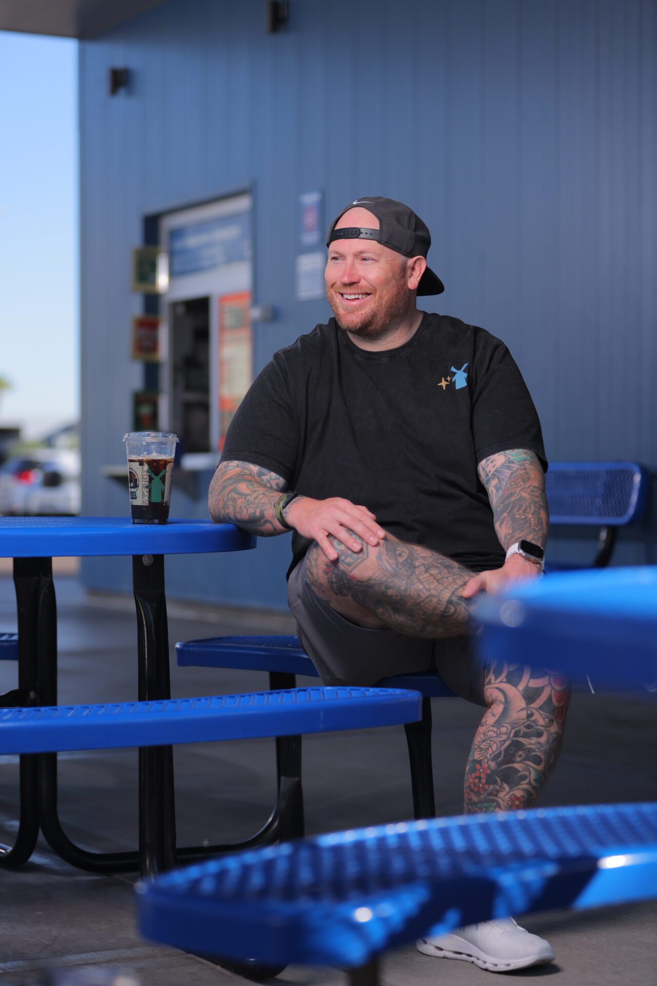 Josh Hayes sits outside of Dutch Bros  with his cup of iced coffee, flashing a smile. 
