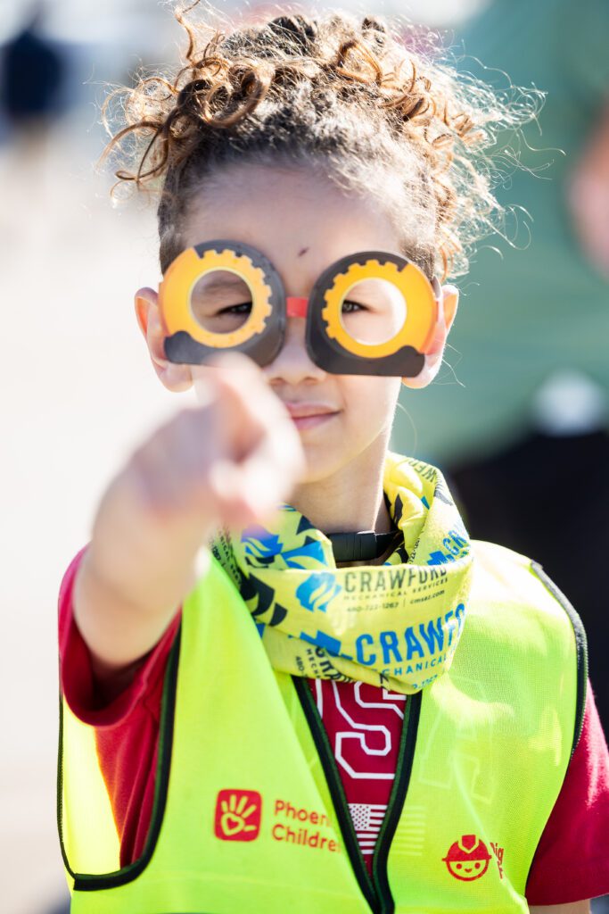 A young girl wears glasses that have construction truck wheels on them at the Big Dig for Kids event.