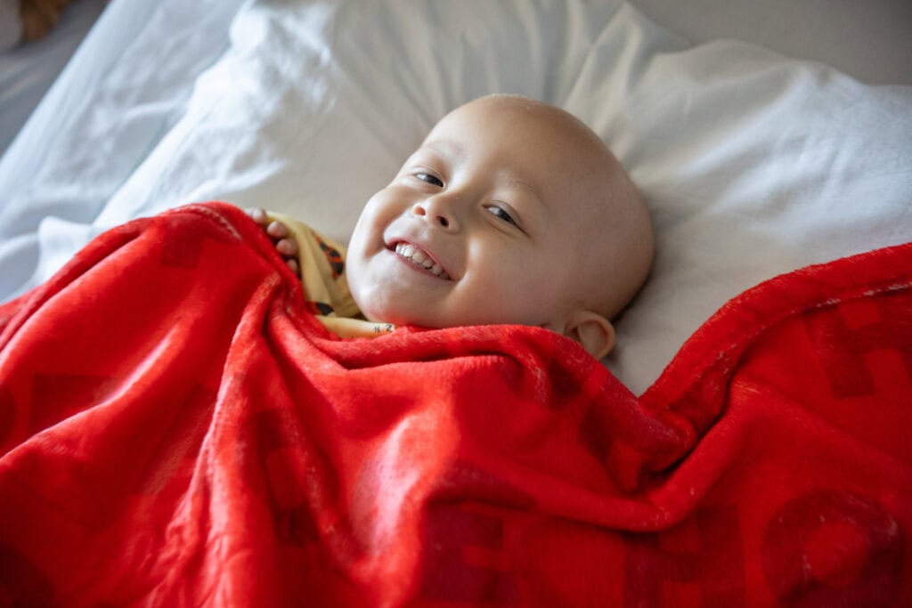 A Phoenix Children's patient snuggles under a red blanket in a hospital bed.