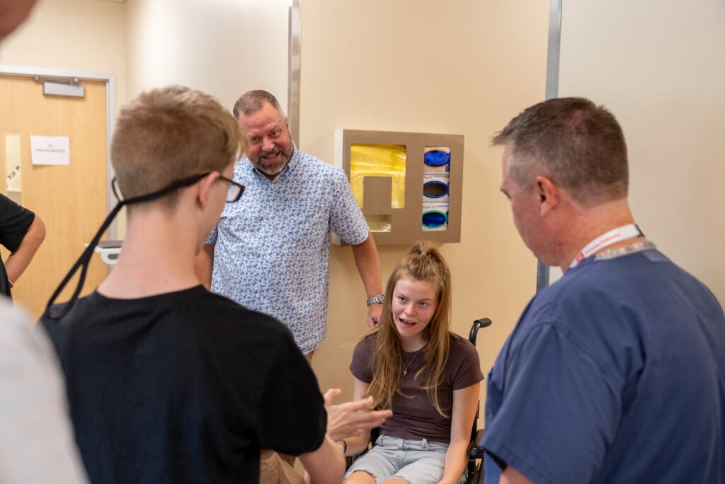 A patient sits in her wheelchair, surrounded by her family and her Phoenix Children's care team.