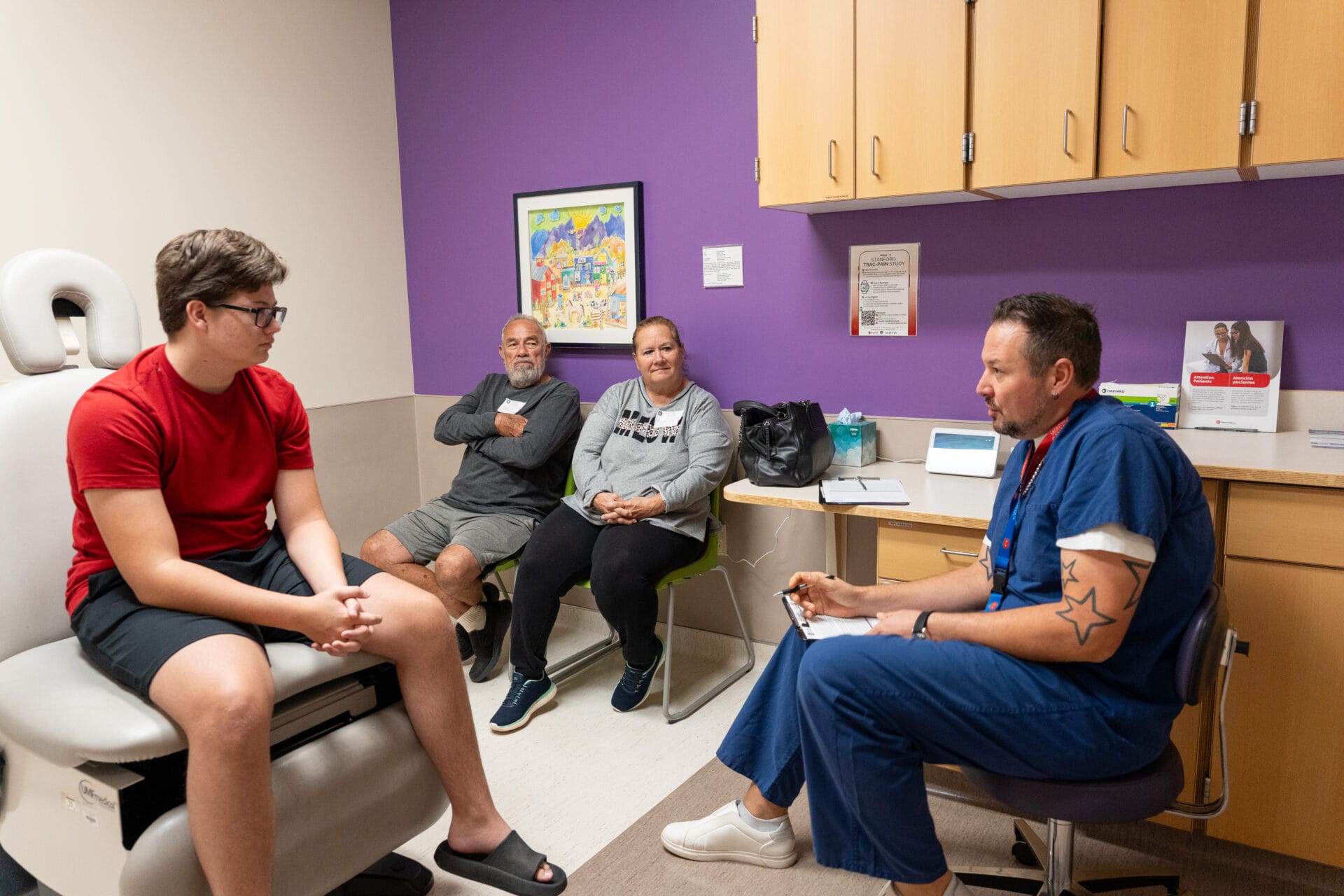 A patient and his parents talk with a doctor in scrubs in an exam room.