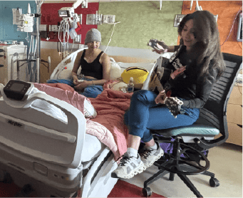 Lily sits in her hospital bed while Jules, her music therapist, plays the guitar at her bedside.