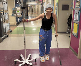 Lily stands in the hospital hallway with her IV stand.