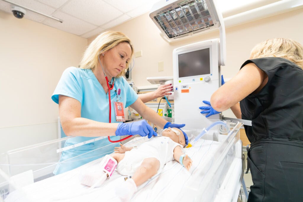 A member of the care team listens to a manikin's heart during a simulation.